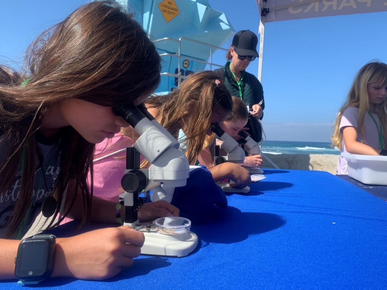 Summer Learning Program body A group of children are looking through microscopes as an interpreter assists them