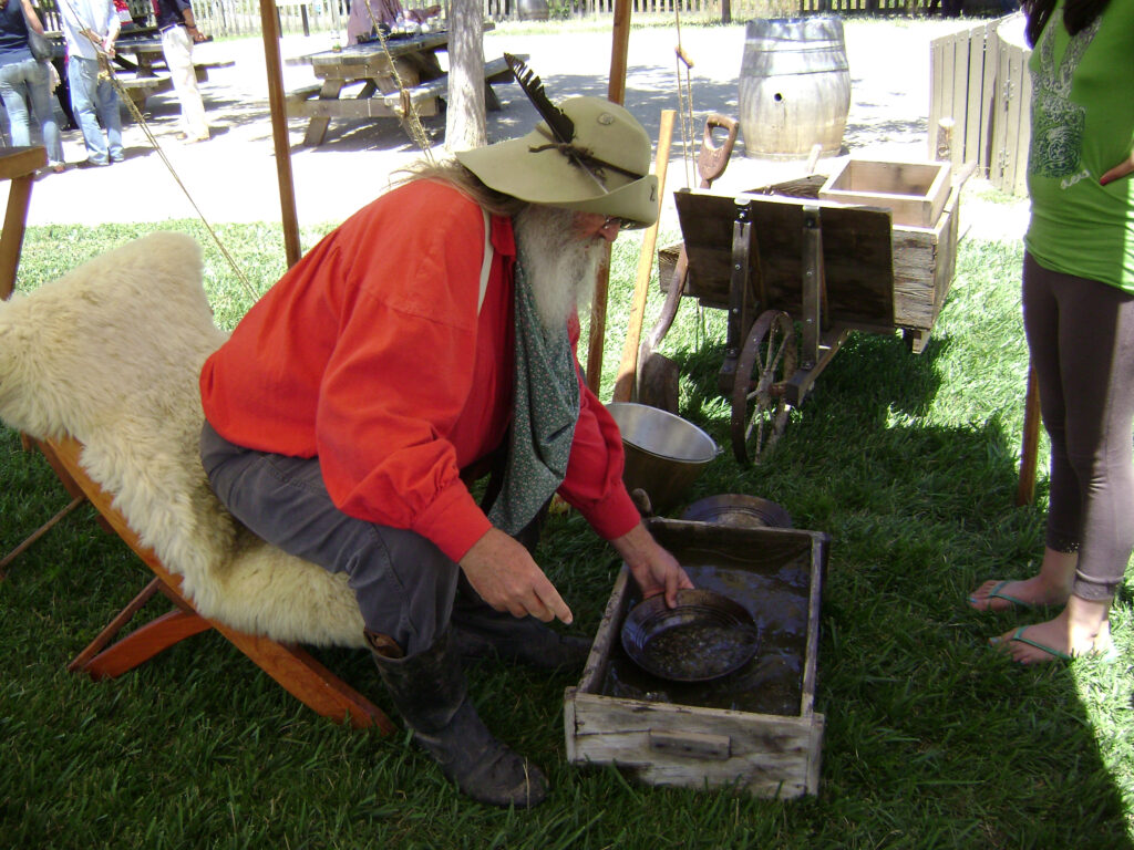 A living history volunteer in historic costume demonstrates gold panning