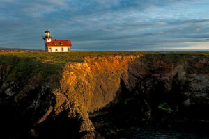 A view of the Point Cabrillo Light station at the edge of a cliff at sunset.