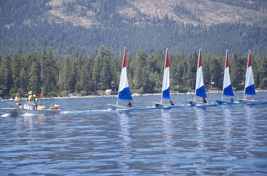 A sailing class on Lake Tahoe - 5 small sailboats with red, white, and blue sails are lined up.