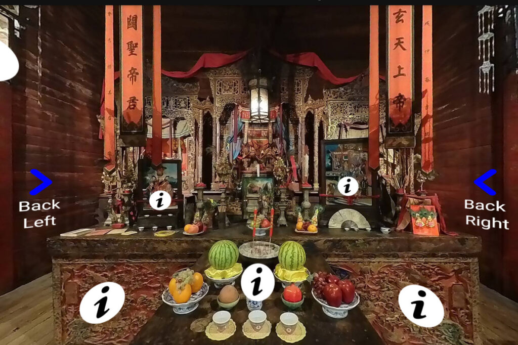 The interior of an Chinese temple. There are food offerings on an altar, incense, and many pieces of art on the altar.