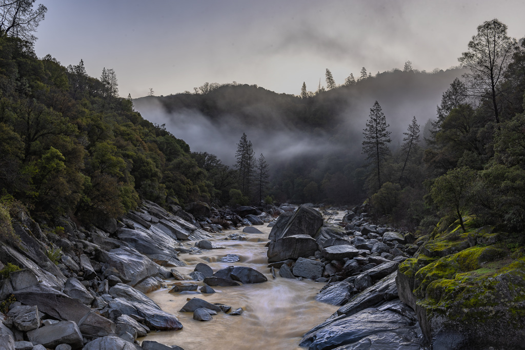 South Yuba River State Park A misty view of the South Yuba River flowing through a rocky gorge surrounded by dense, green forest and tall pine trees in South Yuba River State Park.