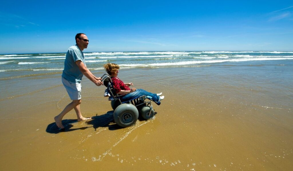 A man is pushing a woman in a beach wheelchair on the beach in Oceano Dunes