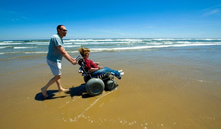A man is pushing a woman in a beach wheelchair on the beach in Oceano Dunes