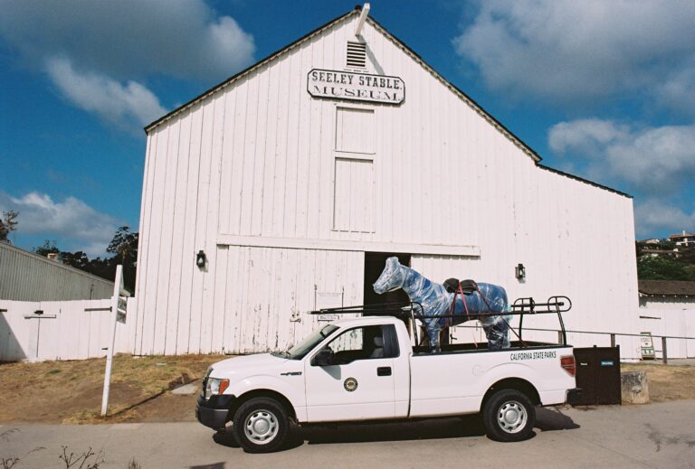 A California State Parks pickup truck with a horse mannequin strapped to the truck bed in front of Seely Stable in Old Town San Diego State Historic Park