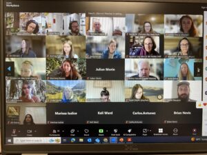 Photograph of a computer screen showing a grid of participant webcam videos in a Zoom meeting.