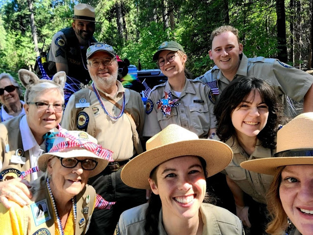 Calaveras Big Trees SP volunteers Risa Fromowitz, Mary Kelly, Bill Minkel, Ford Richards, Linda Stack, and Jan Vallotton and staff Antheney Alegre, Abby Savis, Karri Pearcey, and Amber Sprock on the 4th of July. Photo by Amber Sprock. A group of volunteers and uniformed State Parks employees are casually assembled for a selfie-style group photograph outdoors in front of a stand of trees.