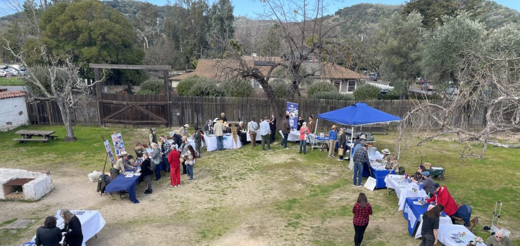 Photograph looking down into the unpaved courtyard of the Sonoma Barracks hosting a semi-circle of staffed outreach tables and visitors