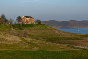 A large brick building stands on a grassy hill overlooking Millerton Lake with rolling hills in the background at Millerton Lake State Recreation Area.