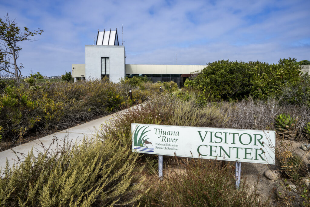 The Tijuana River National Estuarine Research Reserve Visitor Center is surrounded by native coastal plants under a blue sky.