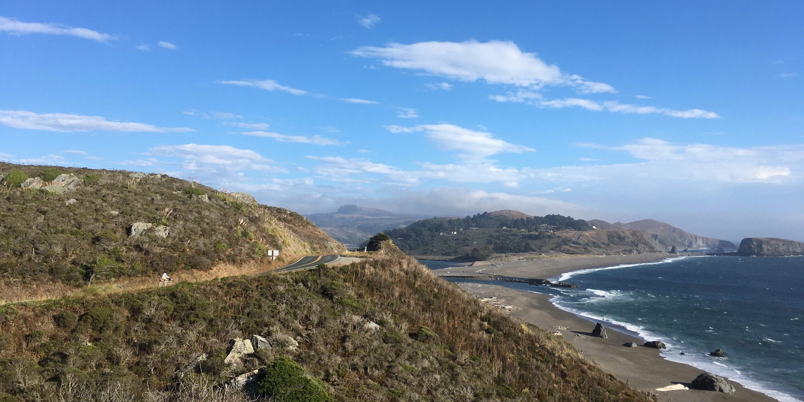 Photograph of Sonoma Coast State Park depicting a cyclist descending California Highway 1 as it winds down a high coastal bluff towards the mouth of the Russian River.