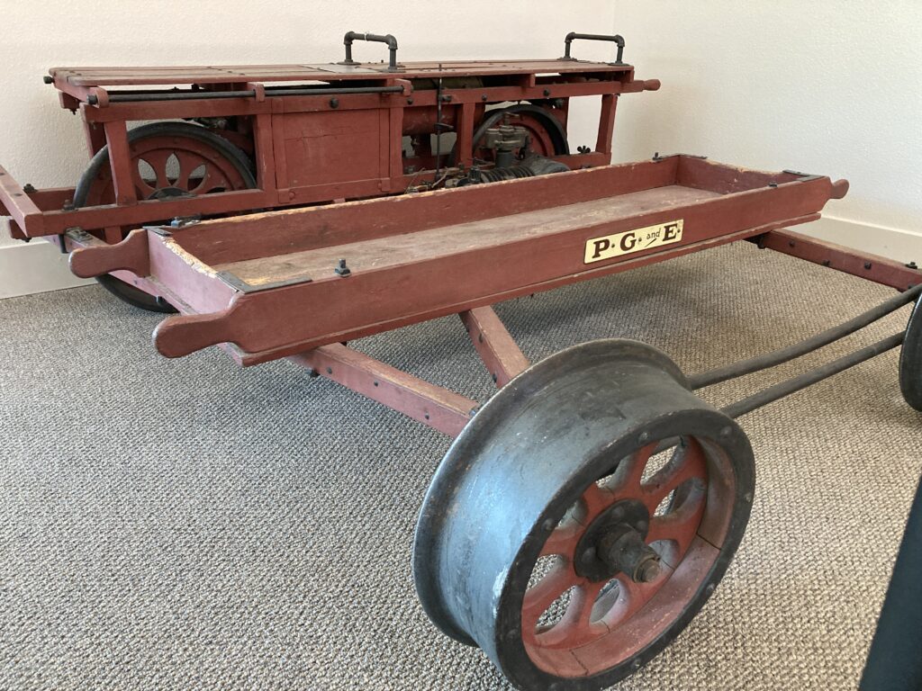 Photograph of an antique gas-powered, wood and metal rail vehicle suitable for 2 riders and a small selction of tools; the car features a placard reading 