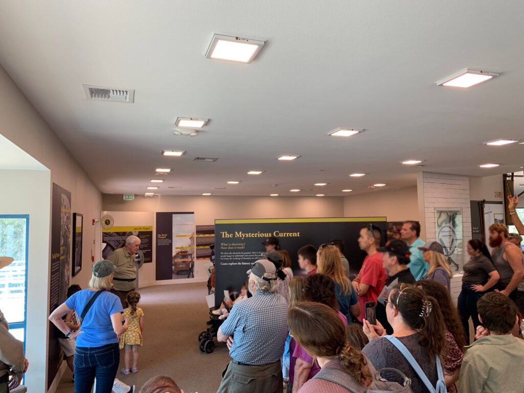 Photograph of the interior of a park Visitor Center depicting a California State Park Docent speaking to a crowd of people.