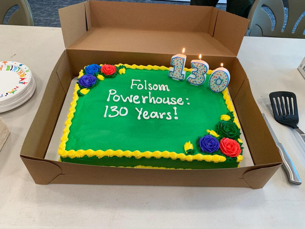 Photograph of a sheet cake decorated in green frosting with three candles spelling out 