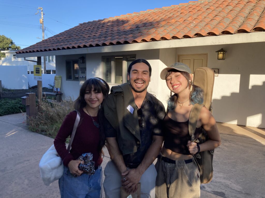 Photograph of three people standing outdoors in front of a stucco walled and tile roofed building.