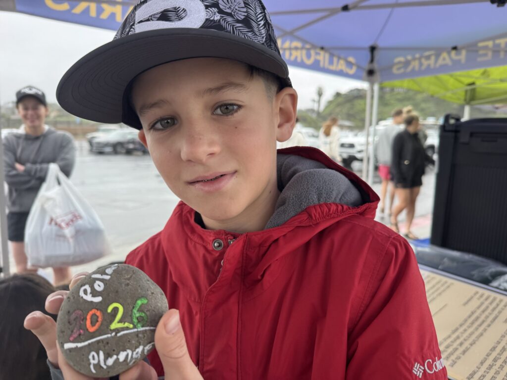 Photograph of a boy holding up a cobblestone painted with the phrase 