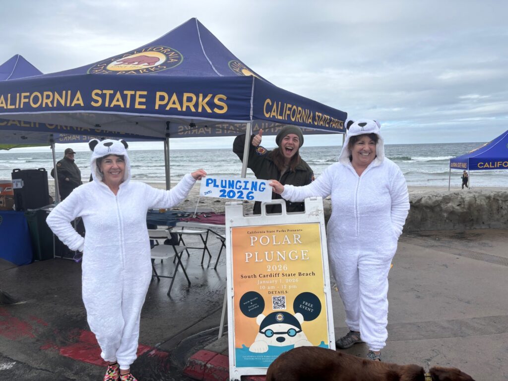 Photo graph of two women dressed in white bear onesies holding a sign reading 