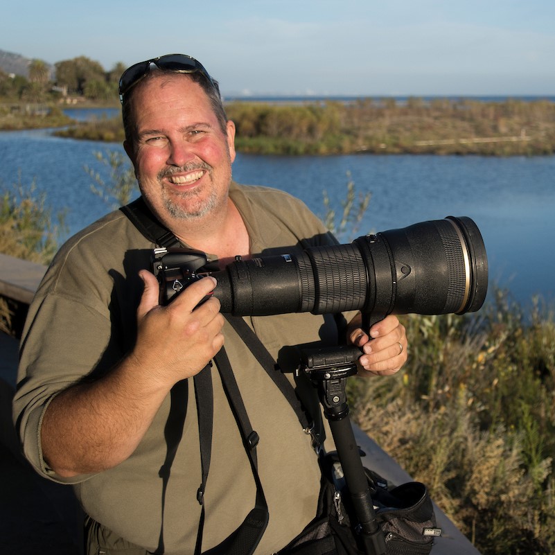 Man supporting camera with long lens on tripod at Malibu Lagoon