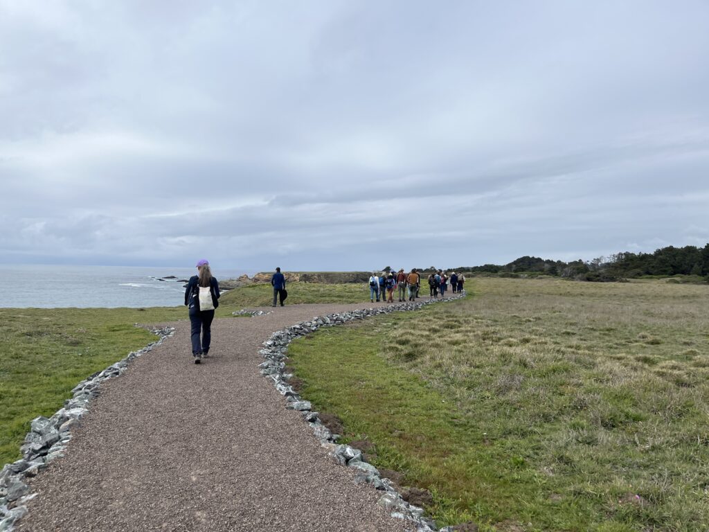 Phototraph of a group of people walking a winding trail atop green coastal bluffs overlooking the ocean