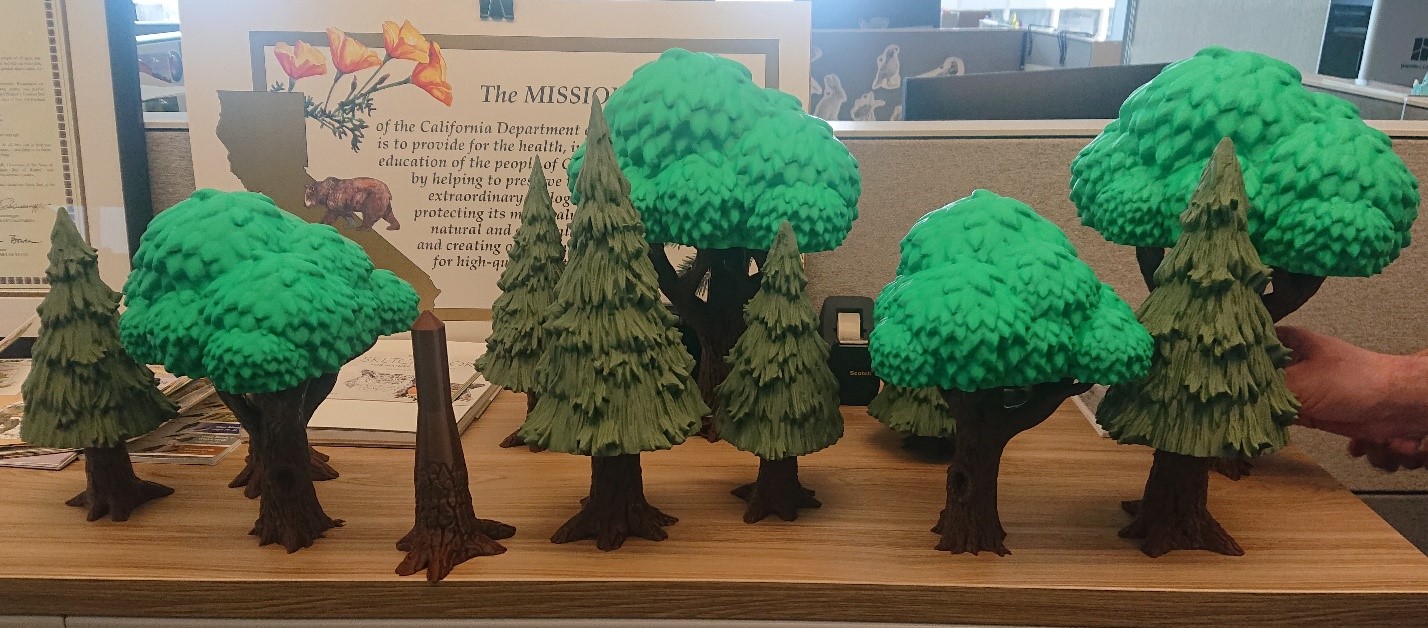 "Trees" created using a 3D printer with two shades of green for foliage and one shade of brown for trunks set up on filing cabinet. 